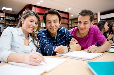 three teens sitting at a table in a library working on a project